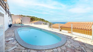 A swimming pool with stone tiles, a fenced area, and a view of the sea.