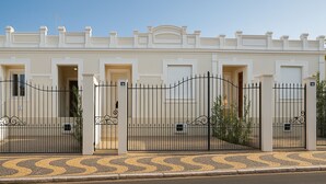 A row of white buildings with numbered doors, black metal gates, and a cobblestone pavement. - Villa Brotas (Brotas)