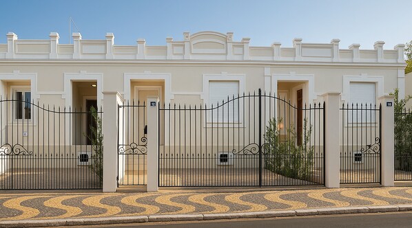 A row of white buildings with numbered doors, black metal gates, and a cobblestone pavement. - Villa Brotas (Brotas)