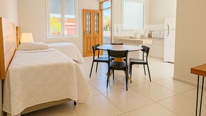 A bedroom with two beds, a small dining area with a table and chairs, and a kitchen area with a refrigerator and microwave. - Villa Brotas (Brotas)