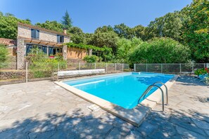 A swimming pool with stone tiles, a stone house with a garden, and a metal fence. - Holiday Home 'Les Taillades' with Shared Pool, Private Terrace and Wi-Fi (Mialet)