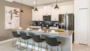 A modern kitchen with a central island, bar stools, pendant lighting, and stainless steel appliances.