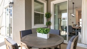 A round patio table with chairs, a white planter with green plants, and a glass door leading to an indoor dining area.