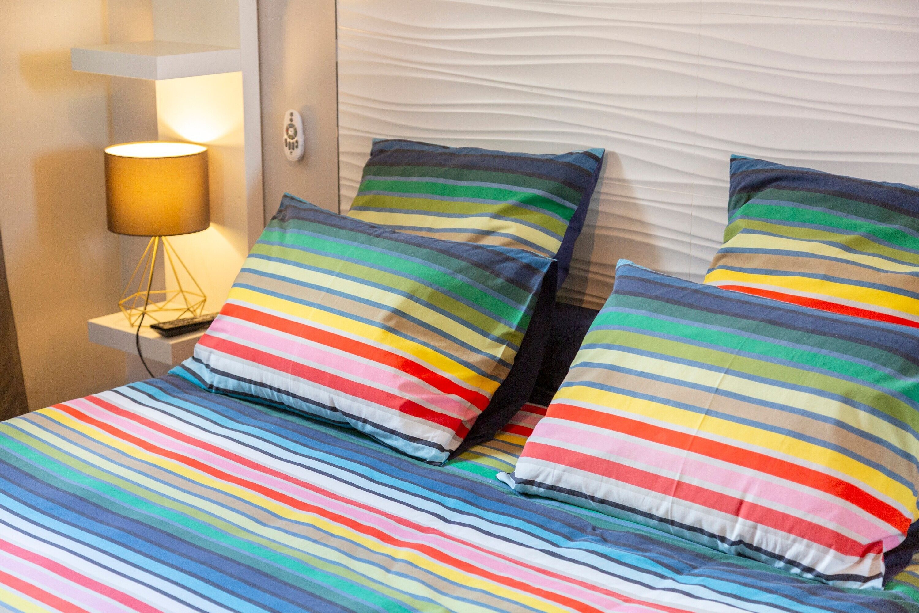 Ein Bett mit gestreifter Bettwäsche und Kissen, eine Nachttischlampe und ein strukturierter Kopfteil.