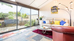 Una sala de estar moderna con un ventanal que da a un jardín, un sofá color beige con cojines de colores, una mesita de centro y una lámpara de pie.