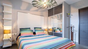 Un dormitorio moderno con colcha a rayas, lámparas de noche, un espejo grande y una lámpara de techo.