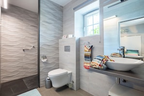 A modern bathroom with a textured wall, a toilet, a sink with a bowl, and a shower area.