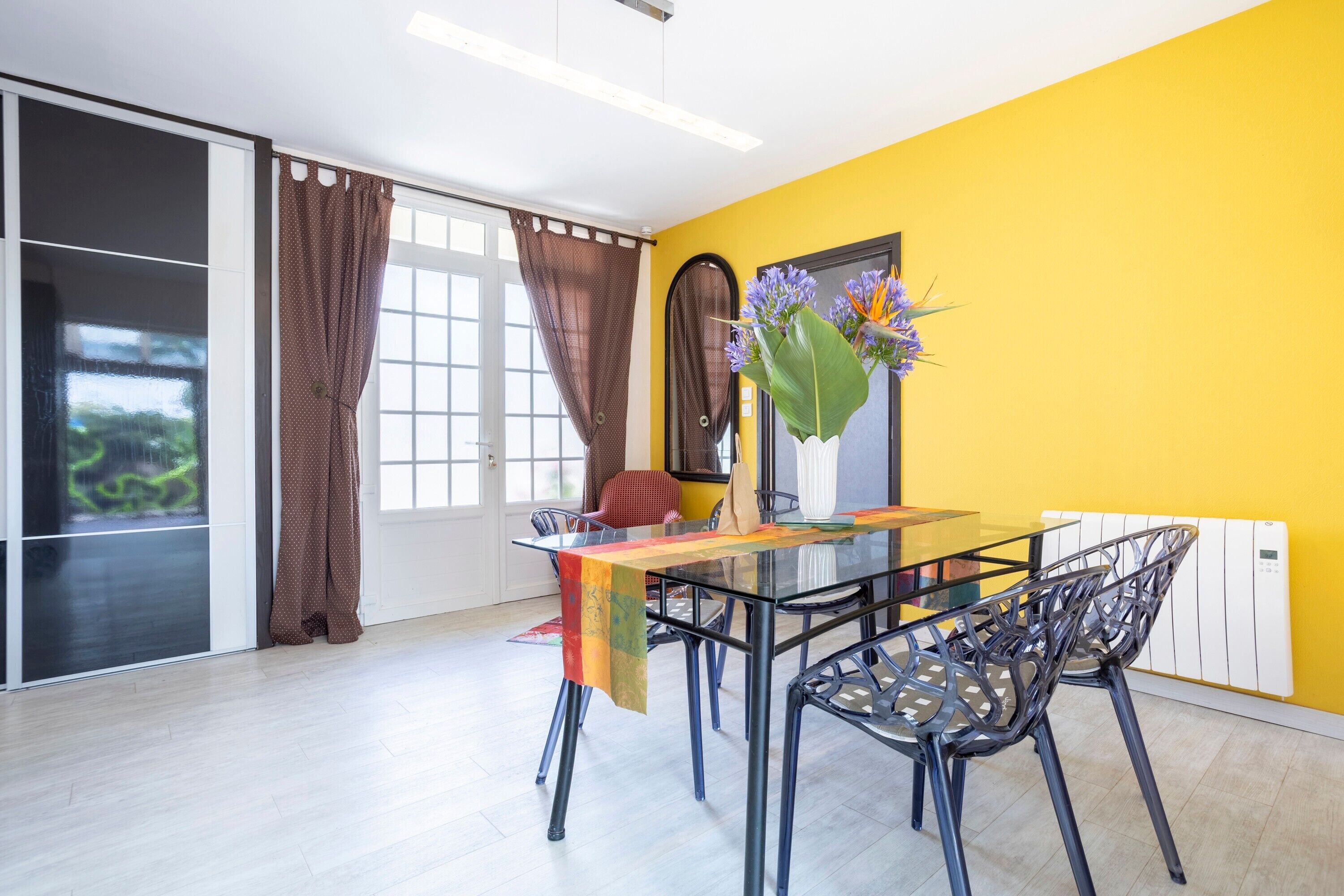 Een eetgedeelte met een glazen tafel, metalen stoelen, een vaas met bloemen, een rode stoel en een schuifpui.