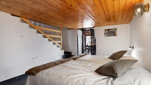 A bedroom with a wooden ceiling, a bed with white bedding, a brown throw blanket, and a staircase.