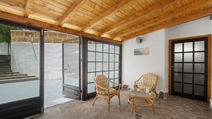 A covered patio area with stone flooring, wicker furniture, and a wooden ceiling.