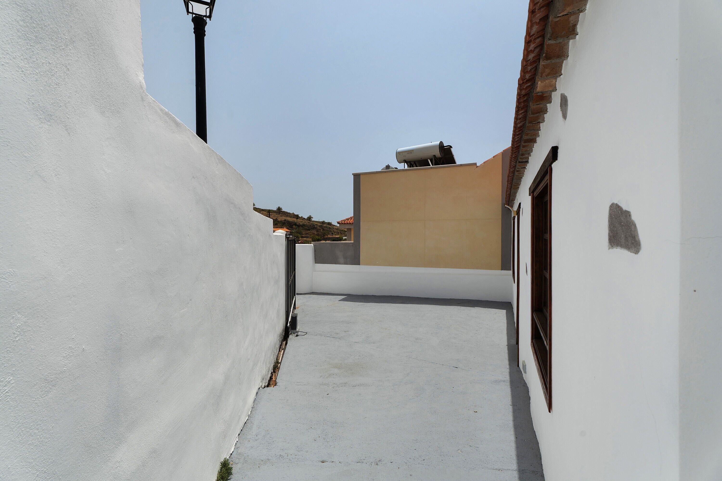 Une ruelle étroite, bordée de bâtiments, avec un mur blanc à gauche et un mur beige à droite.