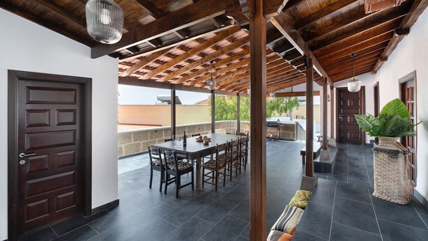 An outdoor patio with a wooden ceiling, a dining table with chairs, a potted plant, and a door.