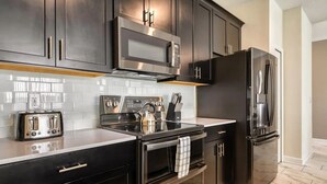 A modern kitchen with dark cabinetry, stainless steel appliances, and a tiled backsplash.