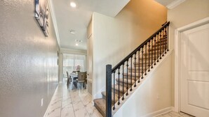 A hallway with a marble floor leading to a staircase with a black balustrade.