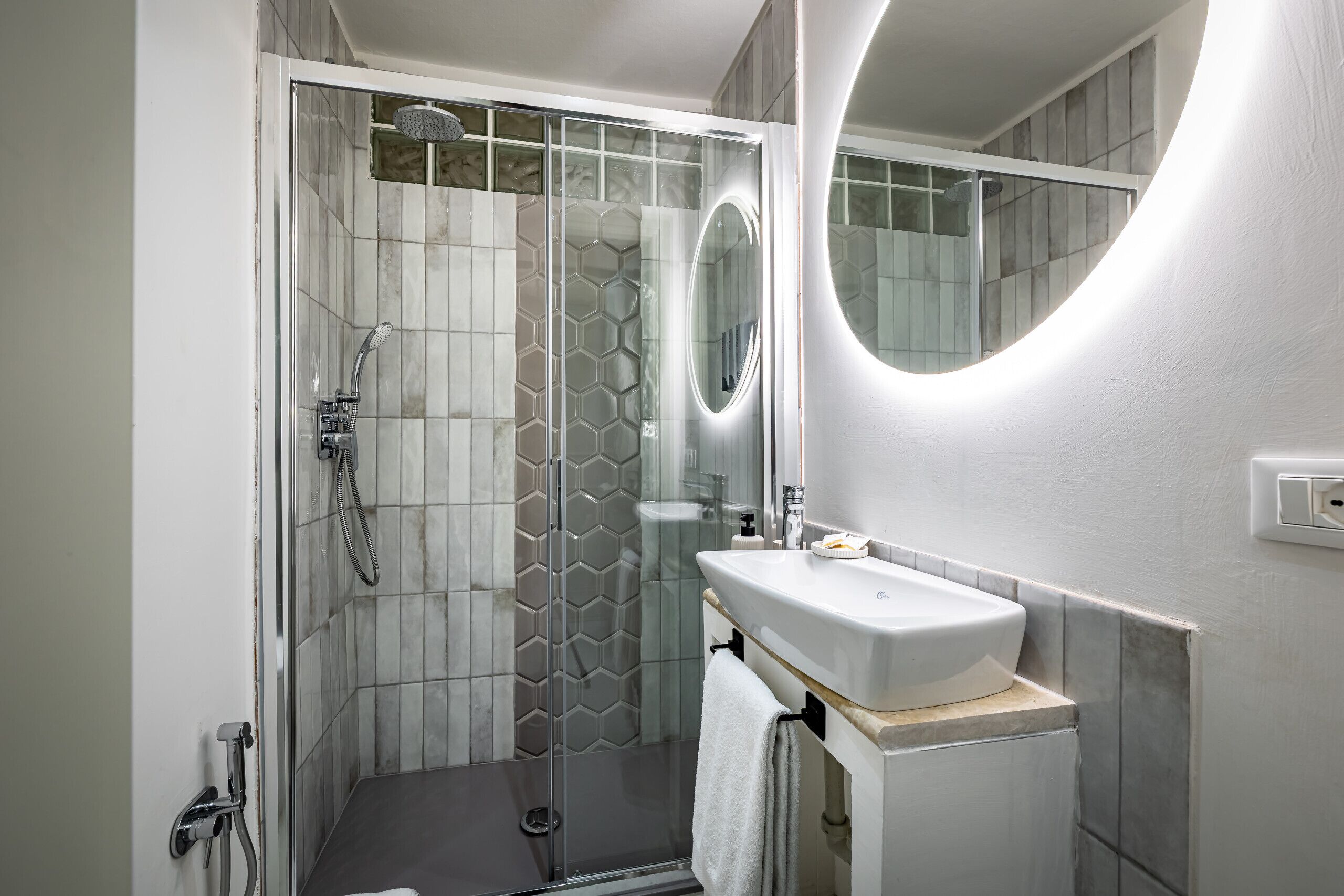 A modern bathroom with a glass-enclosed shower, a white sink, and a large mirror.
