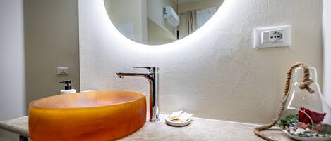 A bathroom with a round mirror, a modern sink, and a decorative glass container with a rope handle.