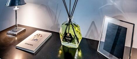 A wall with framed pictures of luxury brands, a table with a lamp, a perfume bottle, and a framed picture.