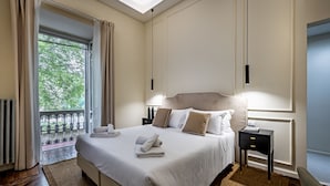 Een netjes ingerichte slaapkamer met een groot bed, een nachtkastje en een uitzicht door een raam op een balkon.