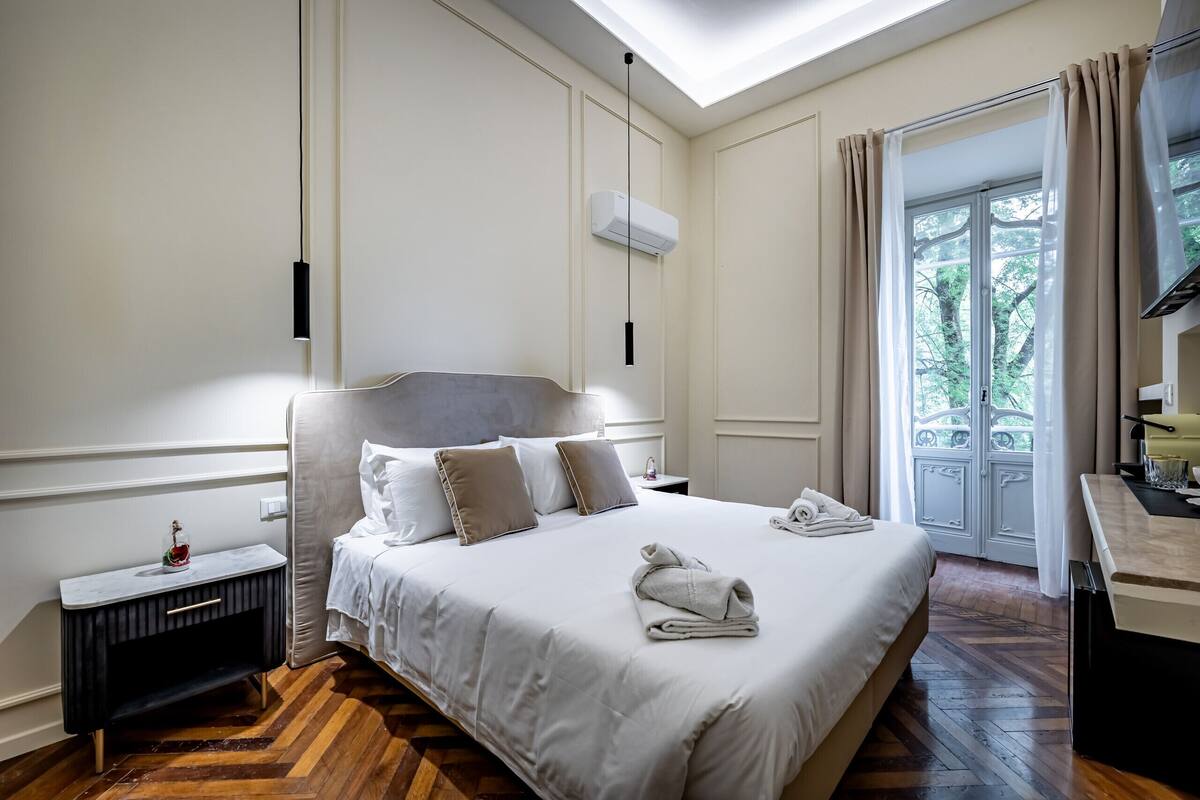 Quarto de hotel com uma cama, mesa de cabeceira e vista para o verde pela janela.