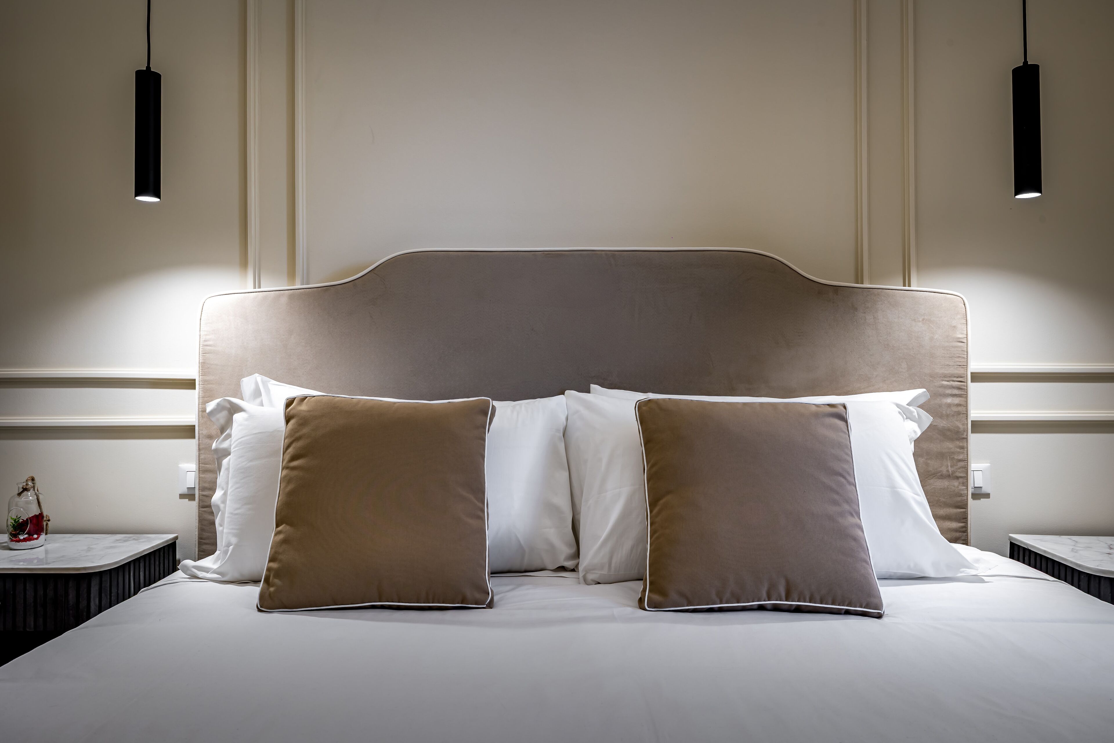 A neatly made bed with a headboard, two bedside tables, and two pendant lights.