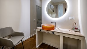Een badkamer met een ronde spiegel, een beige wastafel en een stoel.