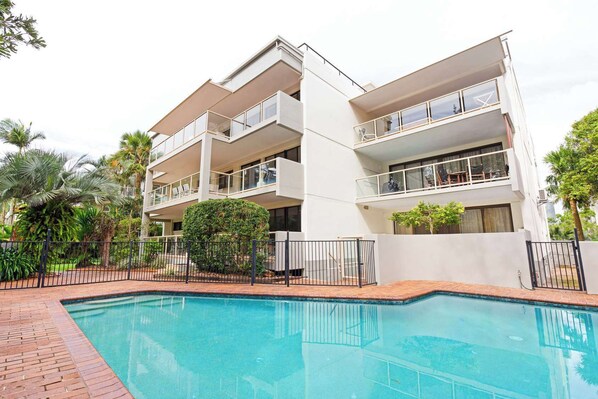 A modern multi-story building with balconies, a swimming pool, and surrounding greenery. - Lahaina 9 Beach Access 60 Seconds (Mooloolaba)
