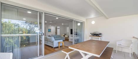 A modern living room with a wooden dining table, a sofa, and a balcony with glass doors.