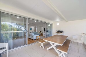 A modern living room with a wooden dining table, a sofa, and a balcony with glass doors. - Lahaina 9 Beach Access 60 Seconds (Mooloolaba)