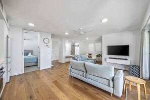 A modern living room with a light blue sofa, a wooden coffee table, and a flat-screen TV mounted on the wall. - Lahaina 9 Beach Access 60 Seconds (Mooloolaba)