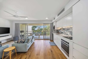 A modern living room with a sofa, TV, and wooden flooring. A balcony with a dining table and chairs is visible. - Lahaina 9 Beach Access 60 Seconds (Mooloolaba)