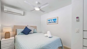 A bedroom with a bed, a ceiling fan, an air conditioner, a bedside table with a lamp, and a framed picture on the wall. - Lahaina 9 Beach Access 60 Seconds (Mooloolaba)
