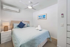 A bedroom with a bed, a ceiling fan, an air conditioner, a bedside table with a lamp, and a framed picture on the wall. - Lahaina 9 Beach Access 60 Seconds (Mooloolaba)