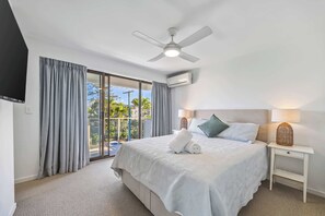 A hotel room with a bed, a ceiling fan, an air conditioning unit, a nightstand with a lamp, and a view of the outdoors through a large window. - Lahaina 9 Beach Access 60 Seconds (Mooloolaba)