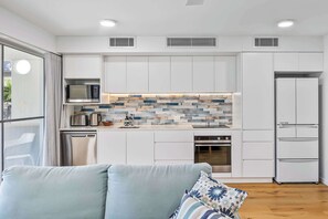 A modern kitchen with white cabinetry, a microwave, a kettle, and a built-in oven. - Lahaina 9 Beach Access 60 Seconds (Mooloolaba)