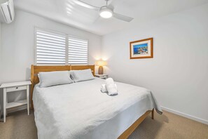 A neatly made bed with white linens, a wooden headboard, a bedside table with a lamp, and a framed picture on the wall. - Lahaina 9 Beach Access 60 Seconds (Mooloolaba)
