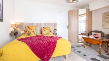 A modern bedroom with a large bed, a wooden headboard, a bedside table with a lamp, and a view of the outside.