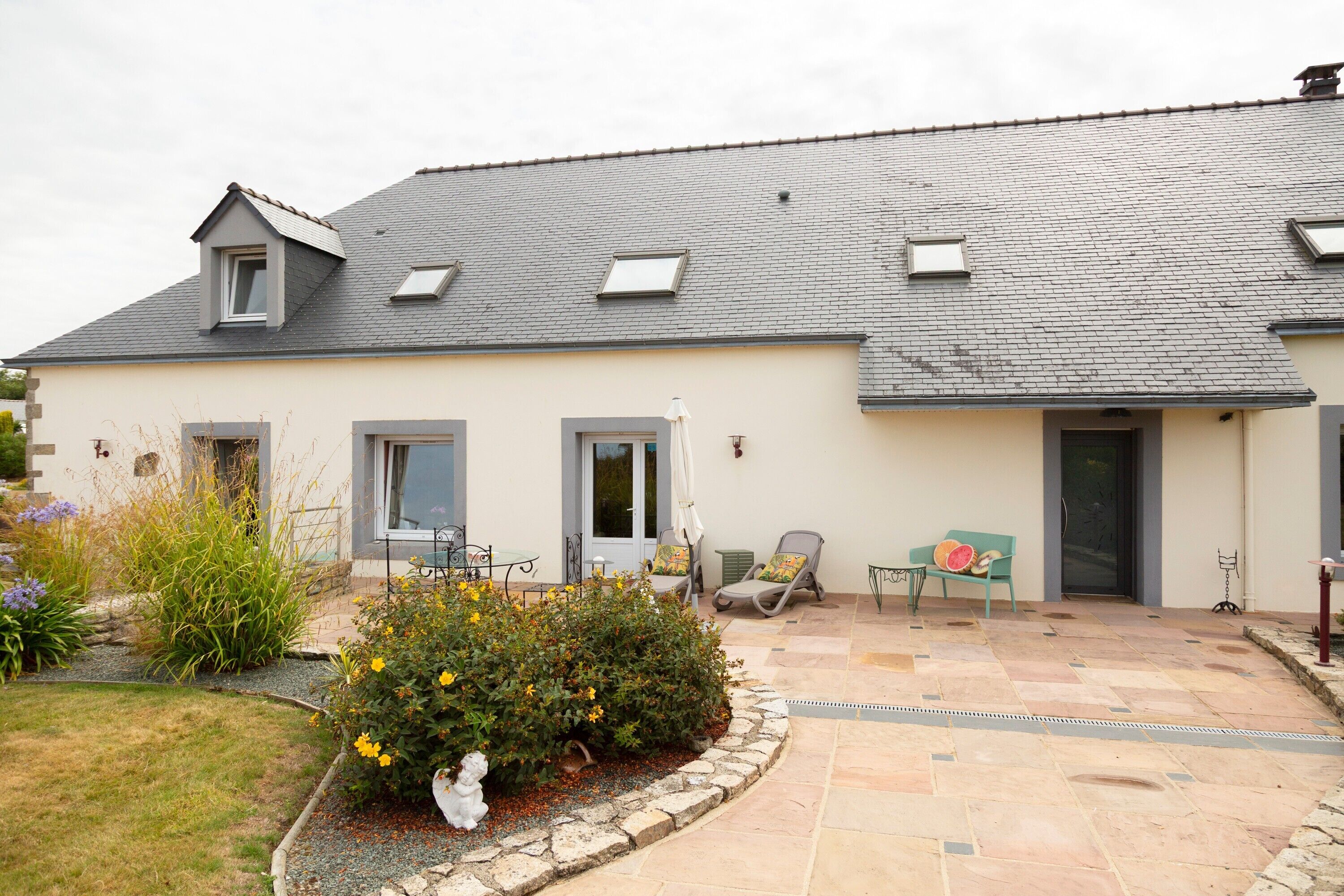 A two-story house with a tiled patio, a small garden, and a door with a window.