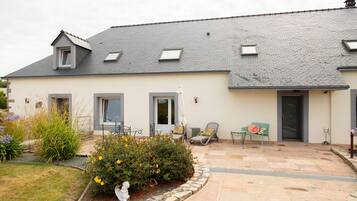 A two-story house with a tiled patio, a small garden, and a door with a window.