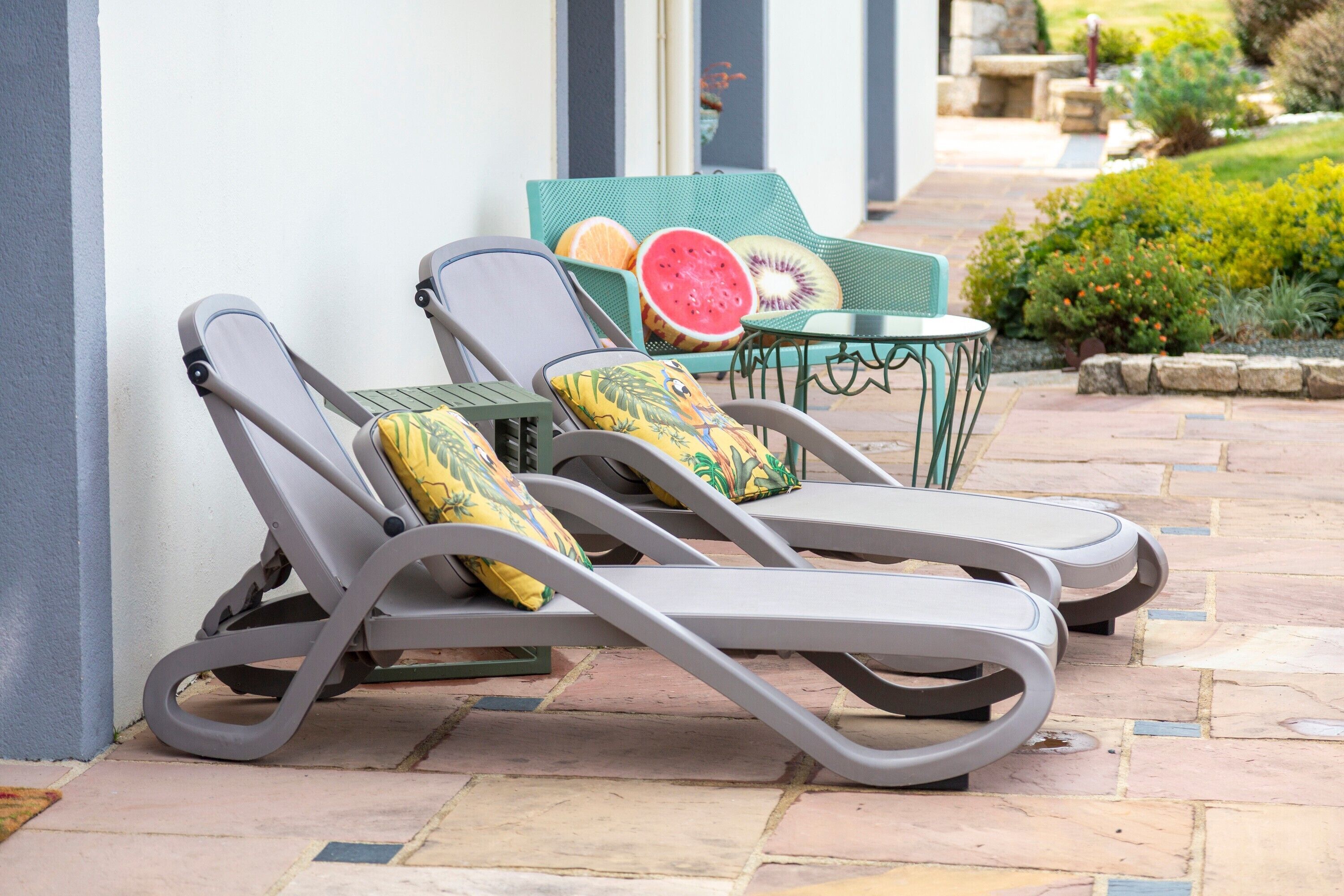 Two lounge chairs with cushions, a small table, and a watermelon slice on a patio.