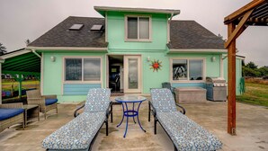 Une maison dotée d’un patio couvert comprenant deux chaises longues, une table et un barbecue.