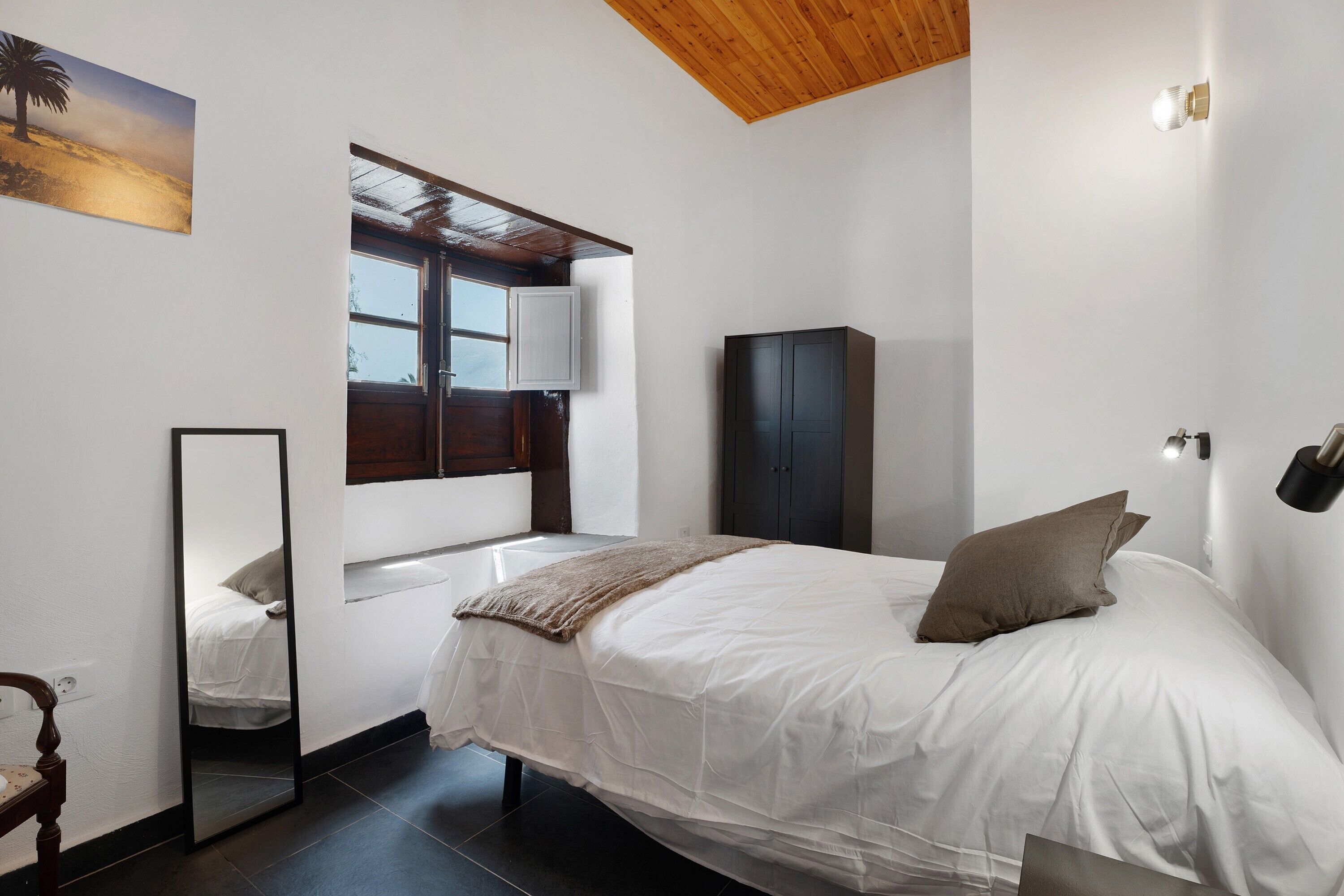 A bedroom with a bed, a wardrobe, a mirror, and a window.