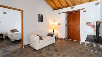 Una habitación con un sofá blanco, una puerta de madera, suelo de piedra y una lámpara.