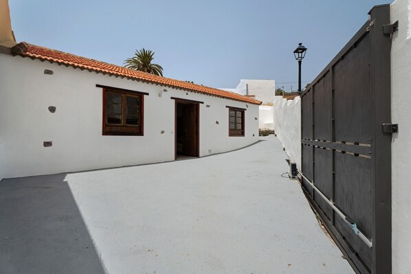 A narrow street with a white building, a closed gate, and a palm tree in the background.
