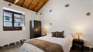 Une chambre à coucher avec un lit, deux tables de chevet avec des lampes, une fenêtre donnant sur un beau paysage et un mur en pierre.