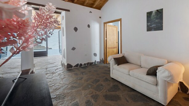 Une pièce avec un sol en pierre, un canapé blanc, une porte en bois et un tableau encadré au mur.