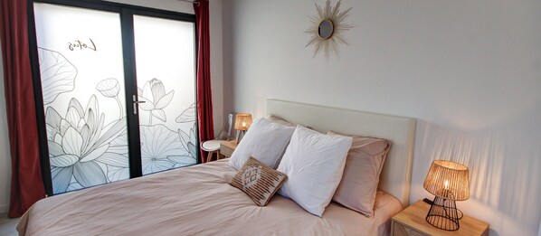 A bedroom with a bed, two pillows, a nightstand with a lamp, and a wall-mounted mirror. - Chambres d'hôtes du Val d'Asson (Montaigu-Vendée)