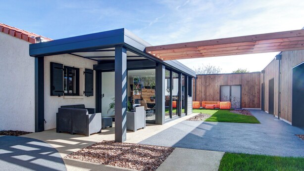 Un patio moderno al aire libre con un área de estar cubierta, una pérgola de madera y un césped bien cuidado.