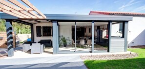 Ett modernt hus med en inglasad uteplats, en matplats och ett kök som syns genom glasdörrar.