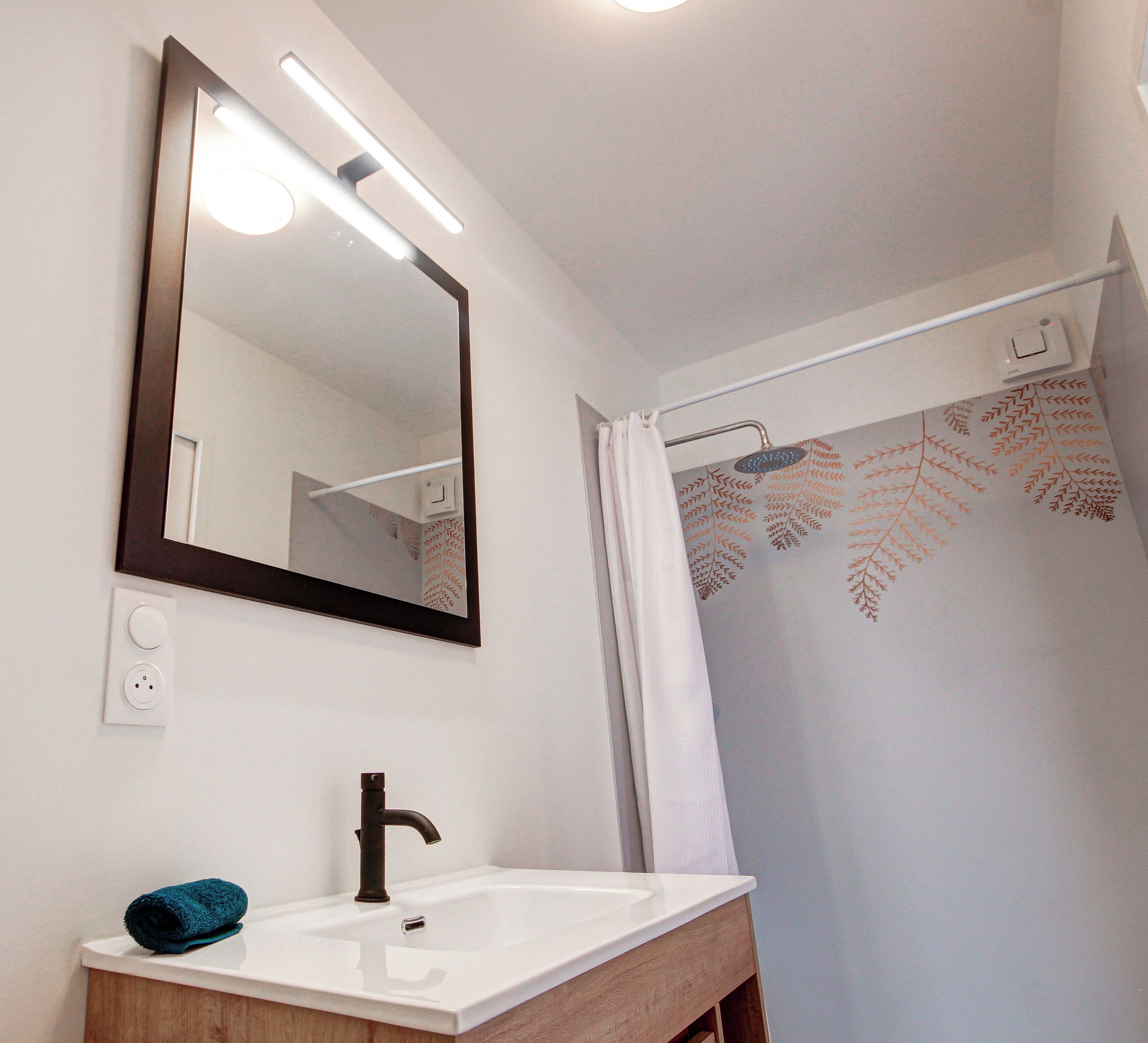A bathroom with a white sink, a mirror, and a shower curtain with a leaf pattern.