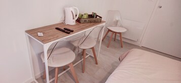 Habitación pequeña con escritorio de madera, dos sillas, una cama, un radiador y una tetera.